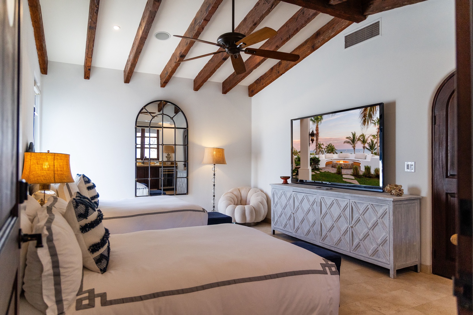 Drift off under dramatic exposed beams in this serene bedroom. Your coastal escape awaits with elegant furnishings, soft lighting, and a flat-screen TV showing ocean views.