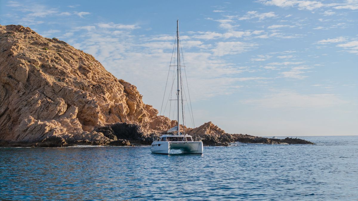 A white catamaran anchored in crystal-clear waters near dramatic golden cliffs creates the perfect Mediterranean escape.
