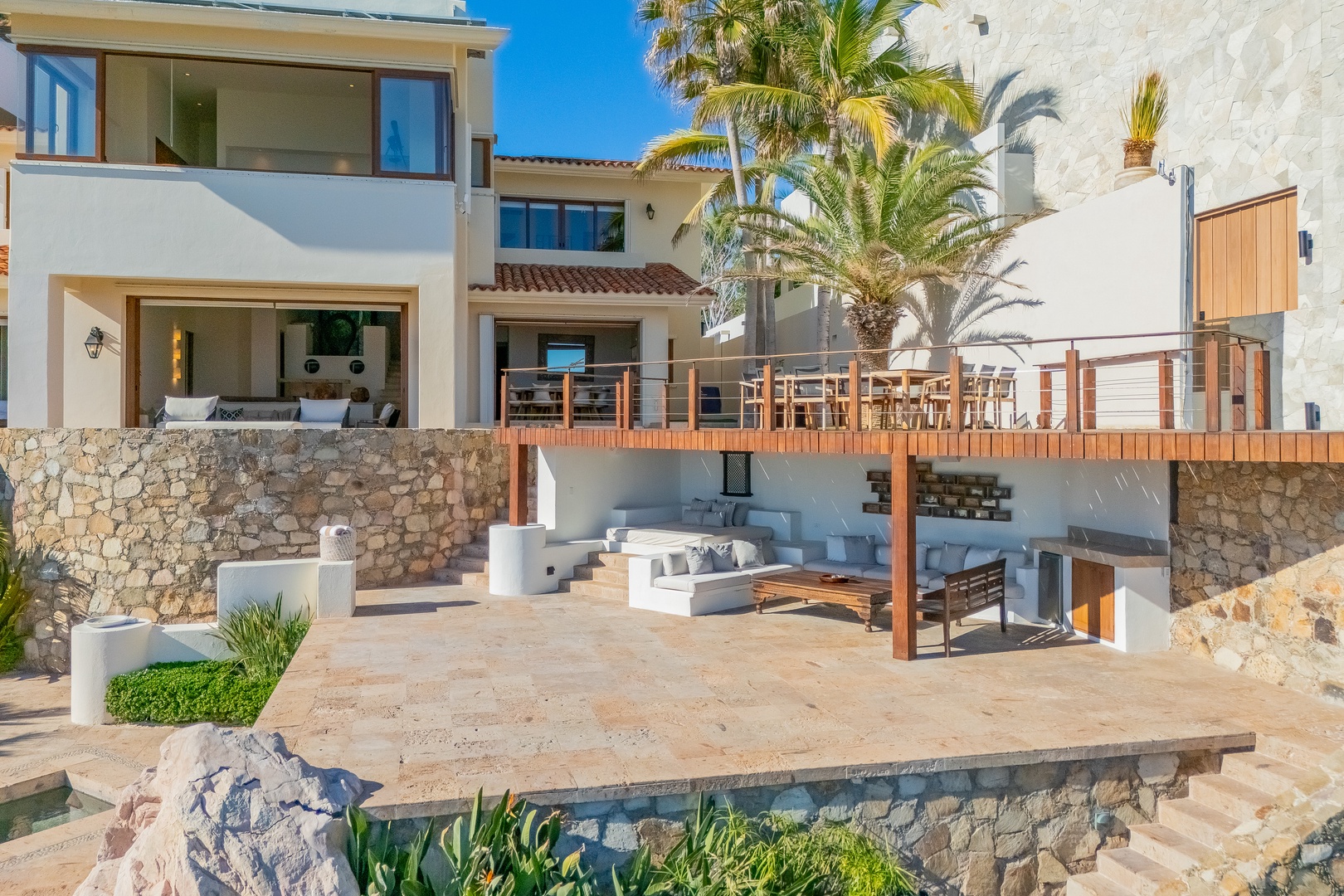 This stunning coastal villa features multi-level terraces, sunlit patios, and tropical palms—an idyllic retreat set against clear blue skies and tranquil ocean views.