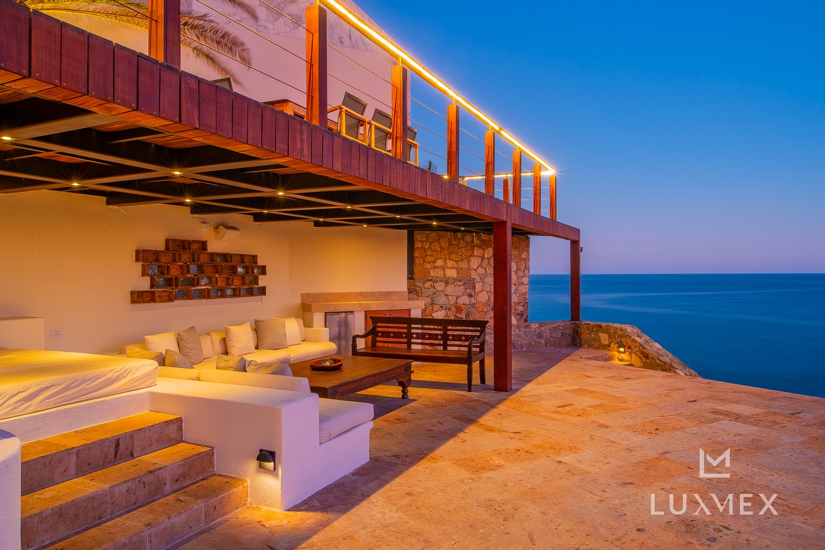 Stunning oceanfront villa with illuminated terraces and infinity views across endless blue waters.