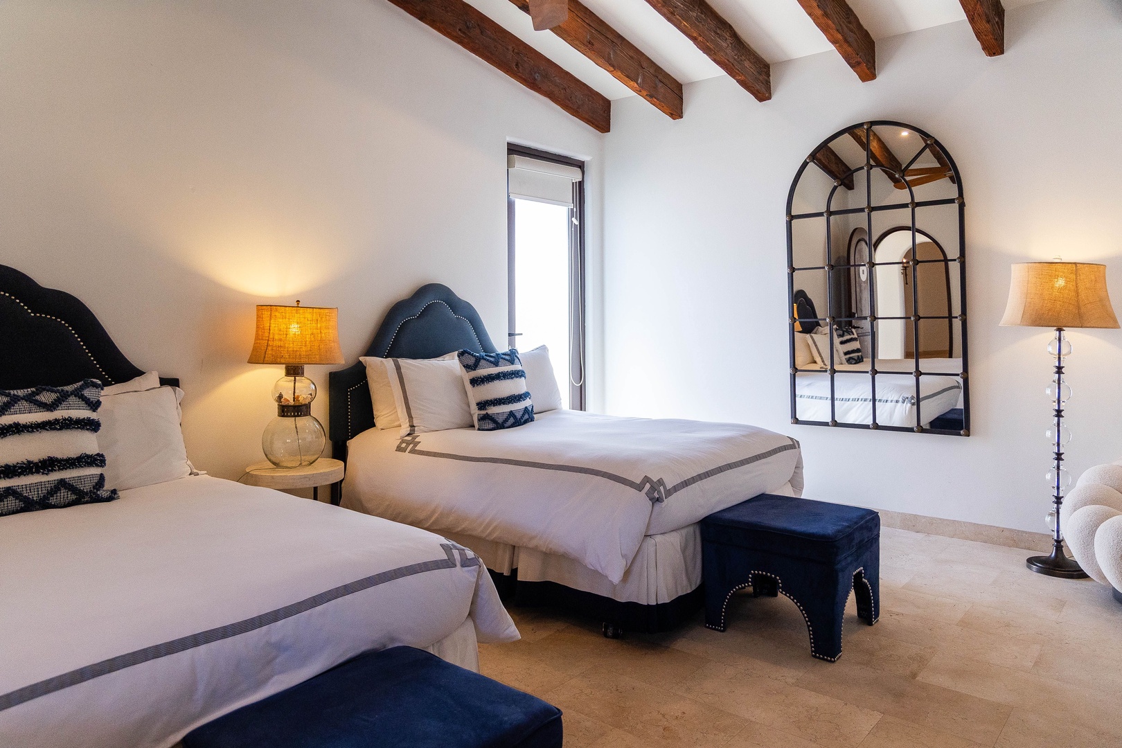 Drift off beneath rustic exposed beams in your dual-bed retreat, where elegant headboards, soft linens, and warm ambient lighting create the perfect restful sanctuary.
