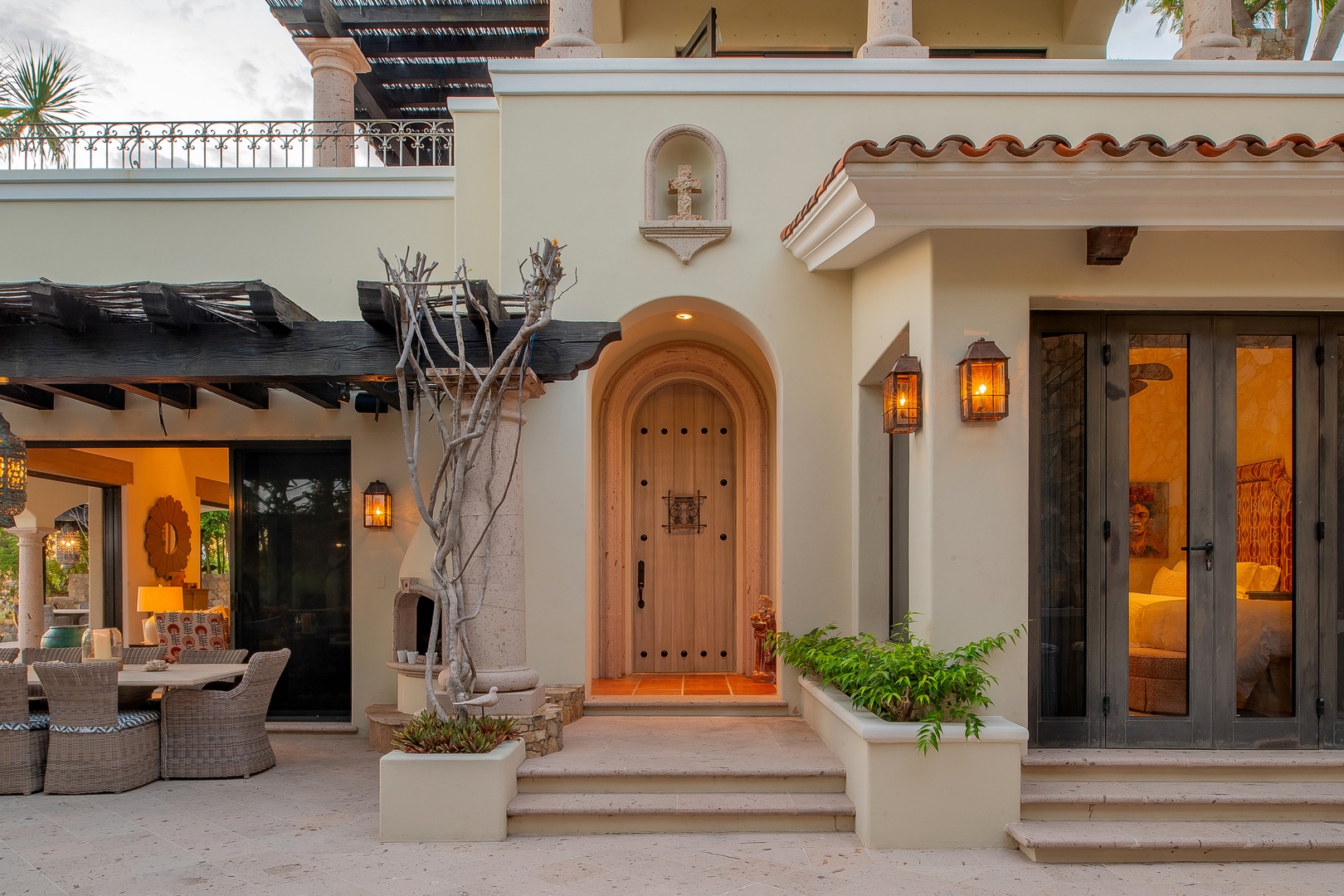 A hacienda-style entrance with arched wooden doors and warm lanterns welcomes you to this elegant coastal retreat, where indoor-outdoor living spaces blend seamlessly into your private patio sanctuary.