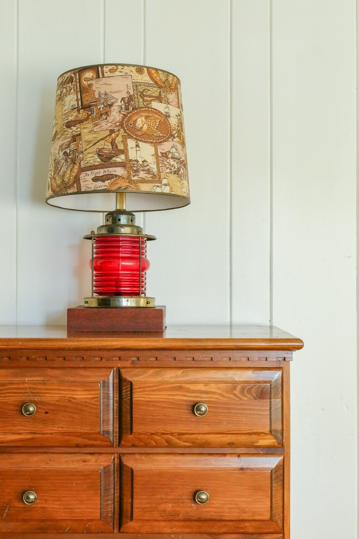 A nautical lamp with vintage maritime illustrations adds character to your bedroom, sitting atop a classic wooden dresser with plenty of storage.