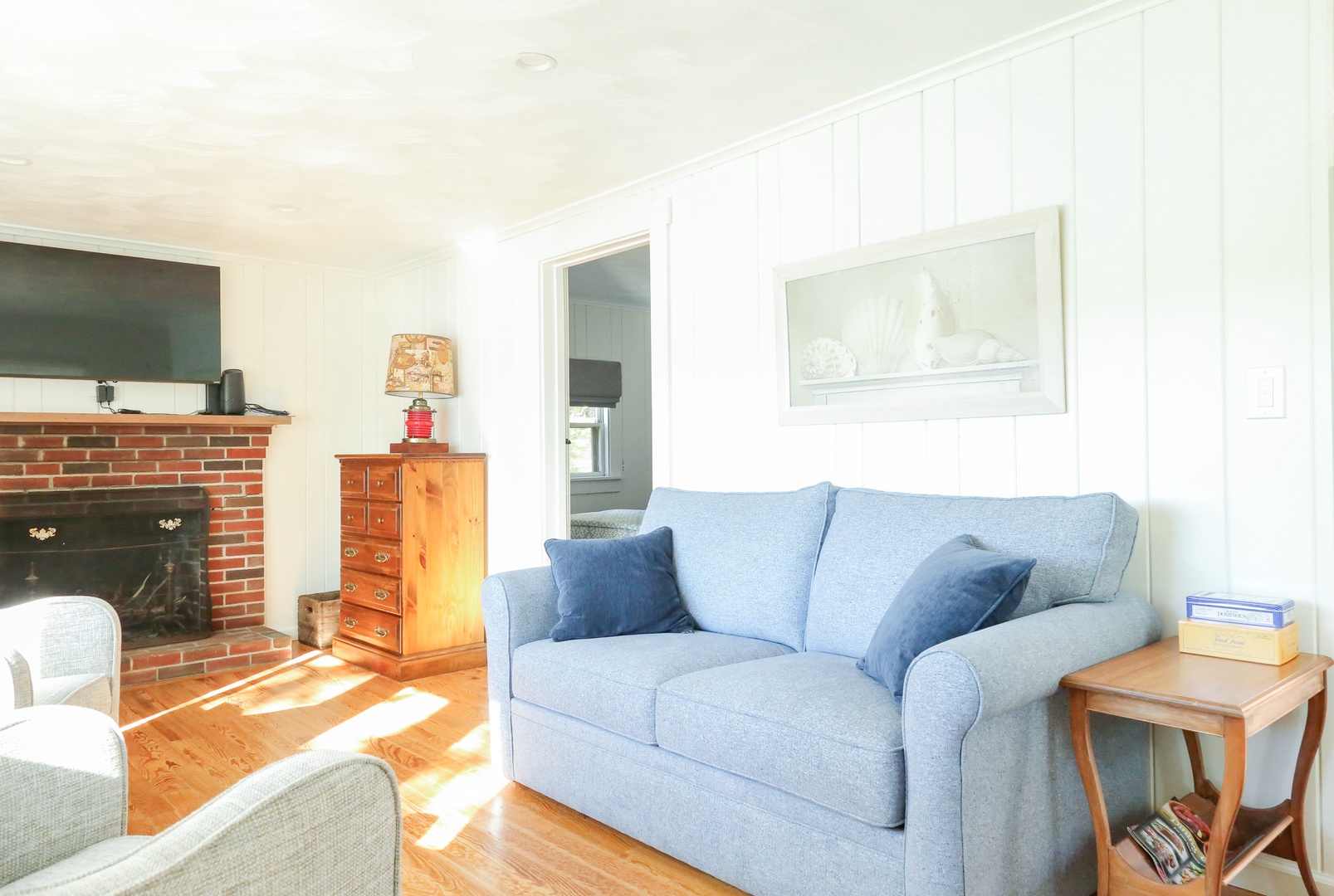 Settle into your cozy living room, where sunlight streams across warm hardwood floors and a charming brick fireplace creates the perfect retreat for relaxing evenings together.