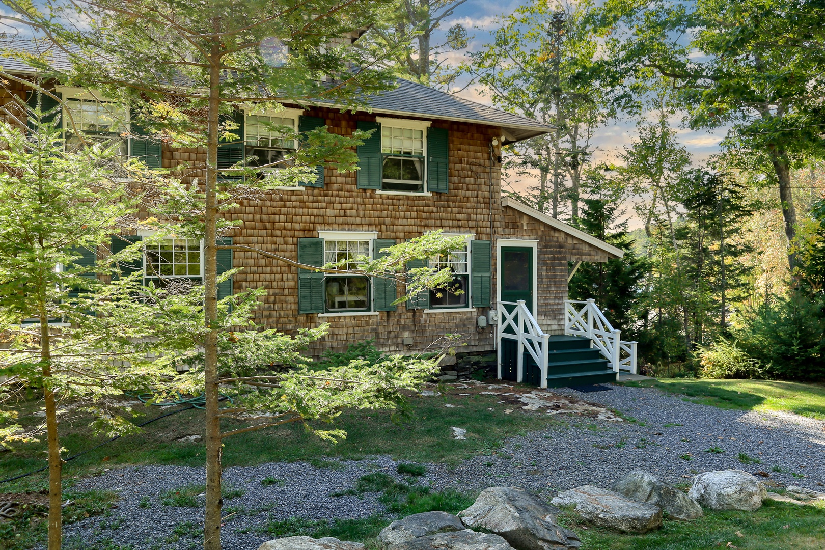 Classic Maine charm awaits at this cedar-shingled cottage, where green shutters and wraparound porches create the perfect waterfront retreat on Linekin Bay.