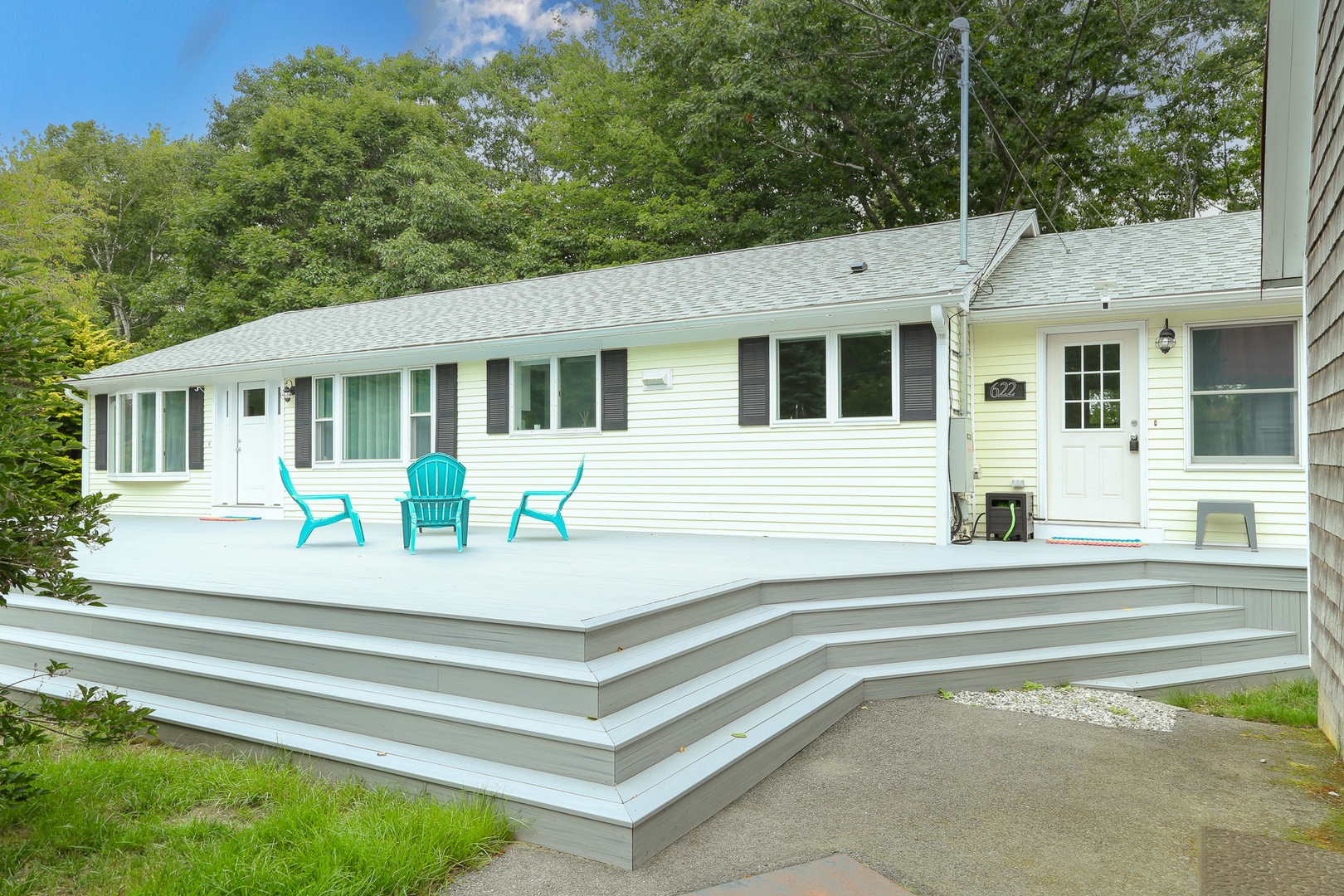 A welcoming home featuring a spacious deck with cheerful turquoise Adirondack chairs, perfectly positioned for enjoying the peaceful natural surroundings.