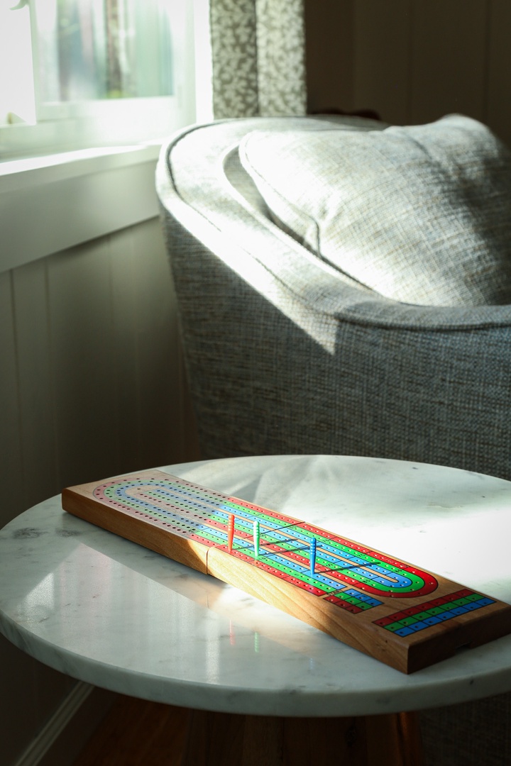 A cribbage board waits on the coffee table, inviting you to unwind in the sunny corner with your favorite game and a cozy seat.