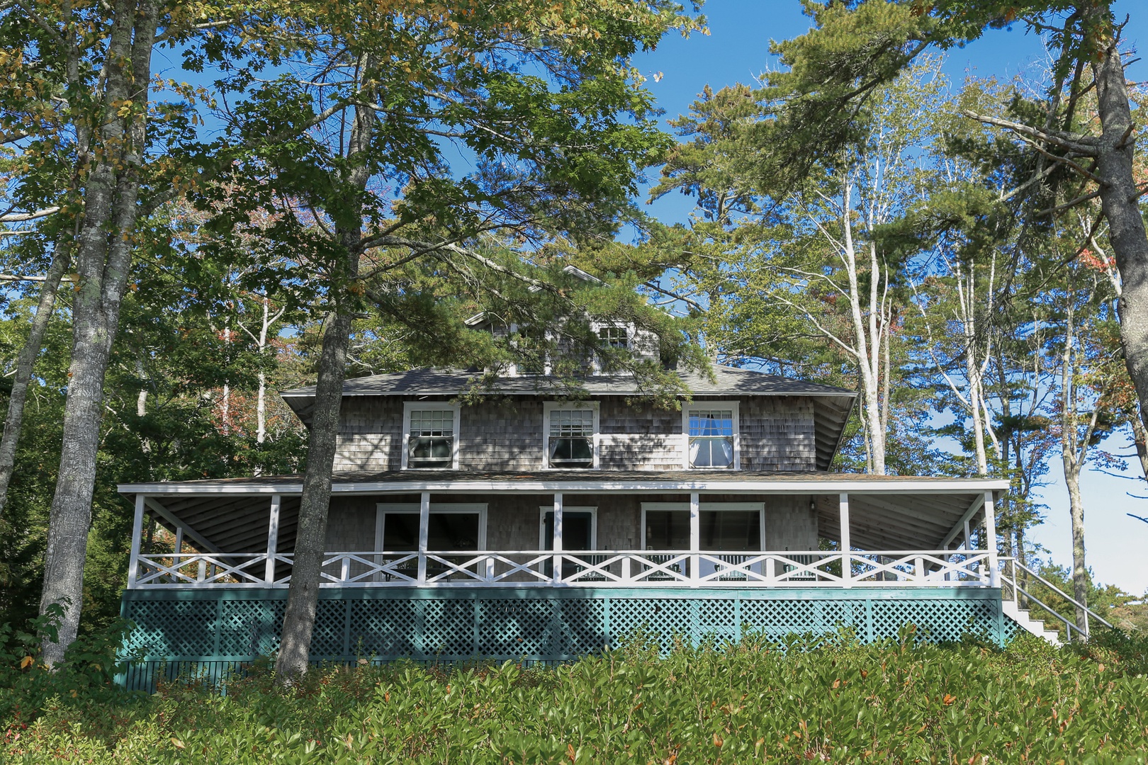 Classic Maine charm awaits at this cedar-shingled cottage, where green shutters and wraparound porches create the perfect waterfront retreat on Linekin Bay.