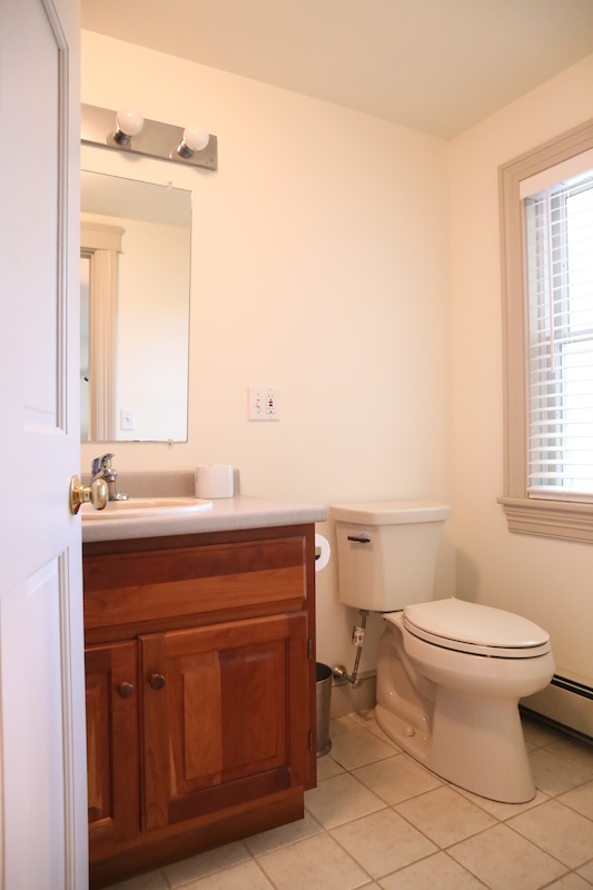 Freshen up in your bright, clean bathroom with classic tile floors, a vanity with warm wood cabinetry, and natural light from the window.