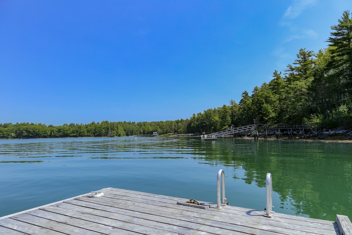 The property features a shared dock extending over the Damariscotta River, surrounded by dense forest and peaceful natural beauty—a perfect waterfront retreat.