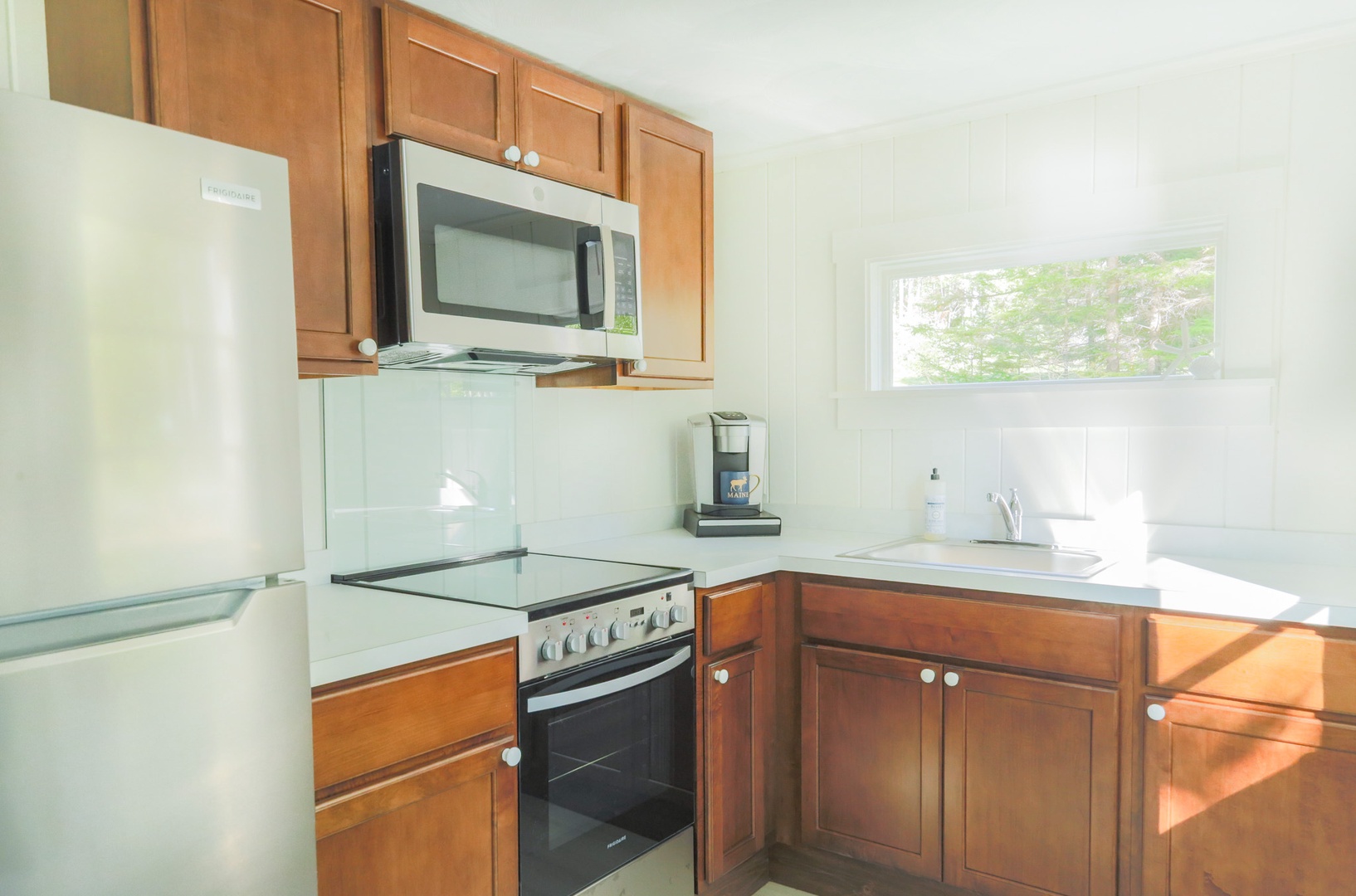 Your fully equipped kitchen features warm wood cabinetry and modern appliances, all bathed in natural light from the window overlooking the greenery outside. Perfect for preparing meals during your stay.