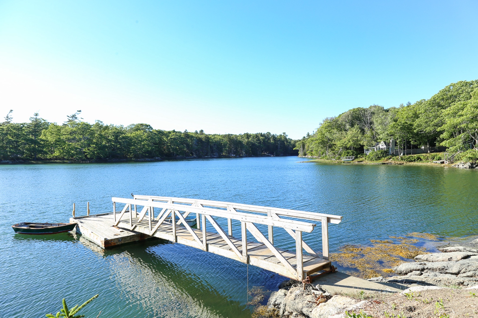 Serene waterfront property offers water access with a private dock and lush natural surroundings under clear blue skies.