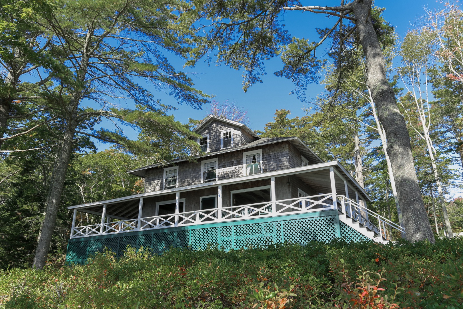 Classic Maine charm awaits at this cedar-shingled cottage, where green shutters and wraparound porches create the perfect waterfront retreat on Linekin Bay.