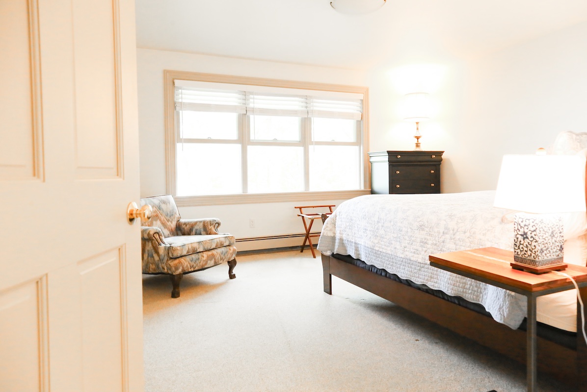Sink into a plush bed in your bright, serene bedroom where soft linens and warm sunlight create a restful retreat. The cozy reading chair invites you to unwind after exploring the area.