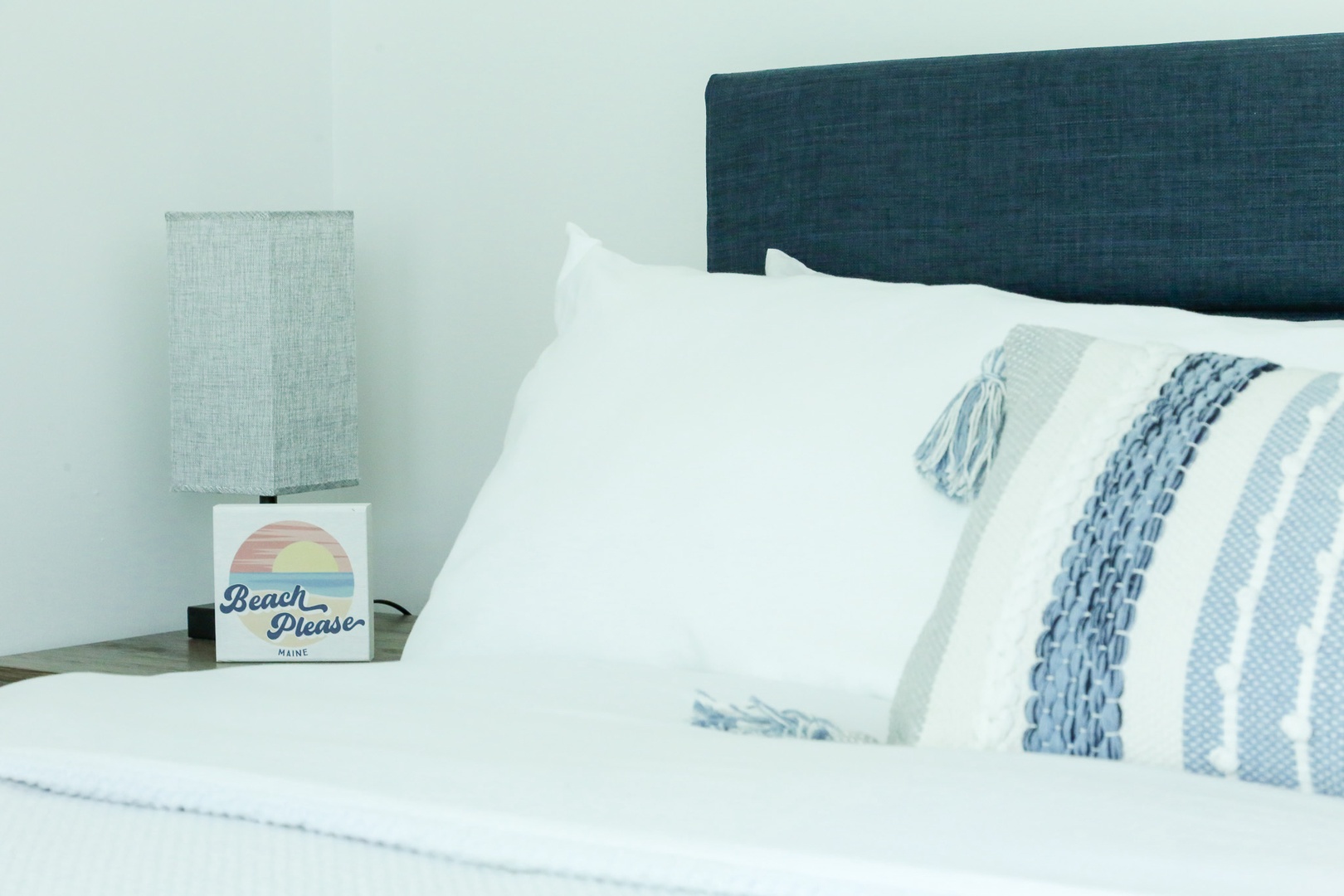 Sink into fresh linens and coastal calm. Your plush bed and bedside lamp invite restful nights by the shore.