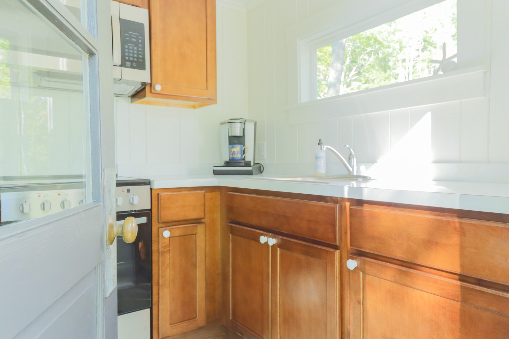 Your sunny kitchen awaits with warm wood cabinetry, a bright window framing leafy views, and a cozy coffee setup ready for easy mornings.