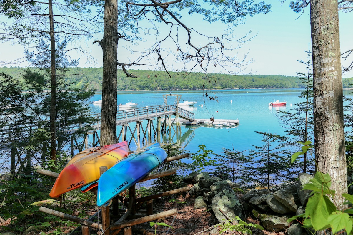Colorful kayaks frame a pristine lake scene with a private dock, perfect for sunrise paddles and afternoon swims. Forest-backed shores and calm waters invite endless summer days on the water.