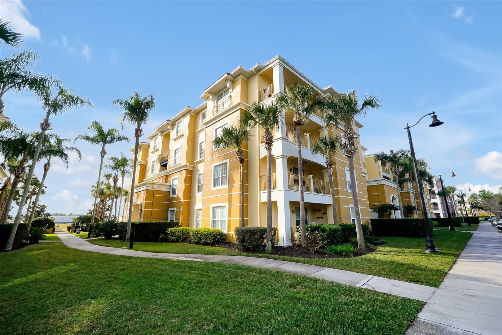 A bright yellow resort building surrounded by lush palm trees and manicured lawns creates a welcoming tropical atmosphere.