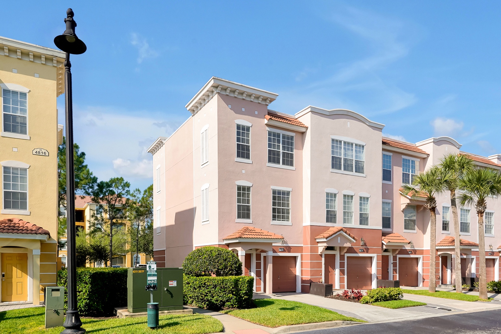 Mediterranean-style townhomes with coral and cream facades feature red tile roofs and palm trees in this sunny residential community.