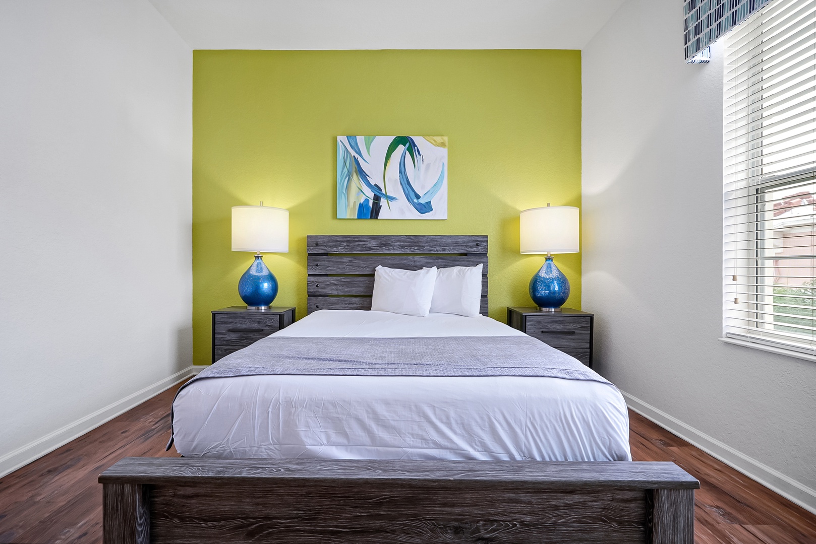 Your bright retreat awaits with a plush bed dressed in crisp linens, framed by glowing bedside lamps and a cheerful accent wall that invites restful sleep.
