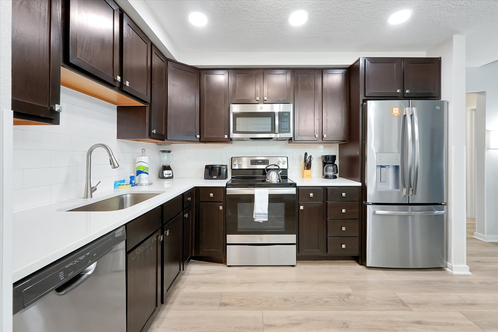 Your fully equipped kitchen features dark wood cabinets, stainless steel appliances, and pristine white countertops—perfect for preparing memorable meals during your stay.
