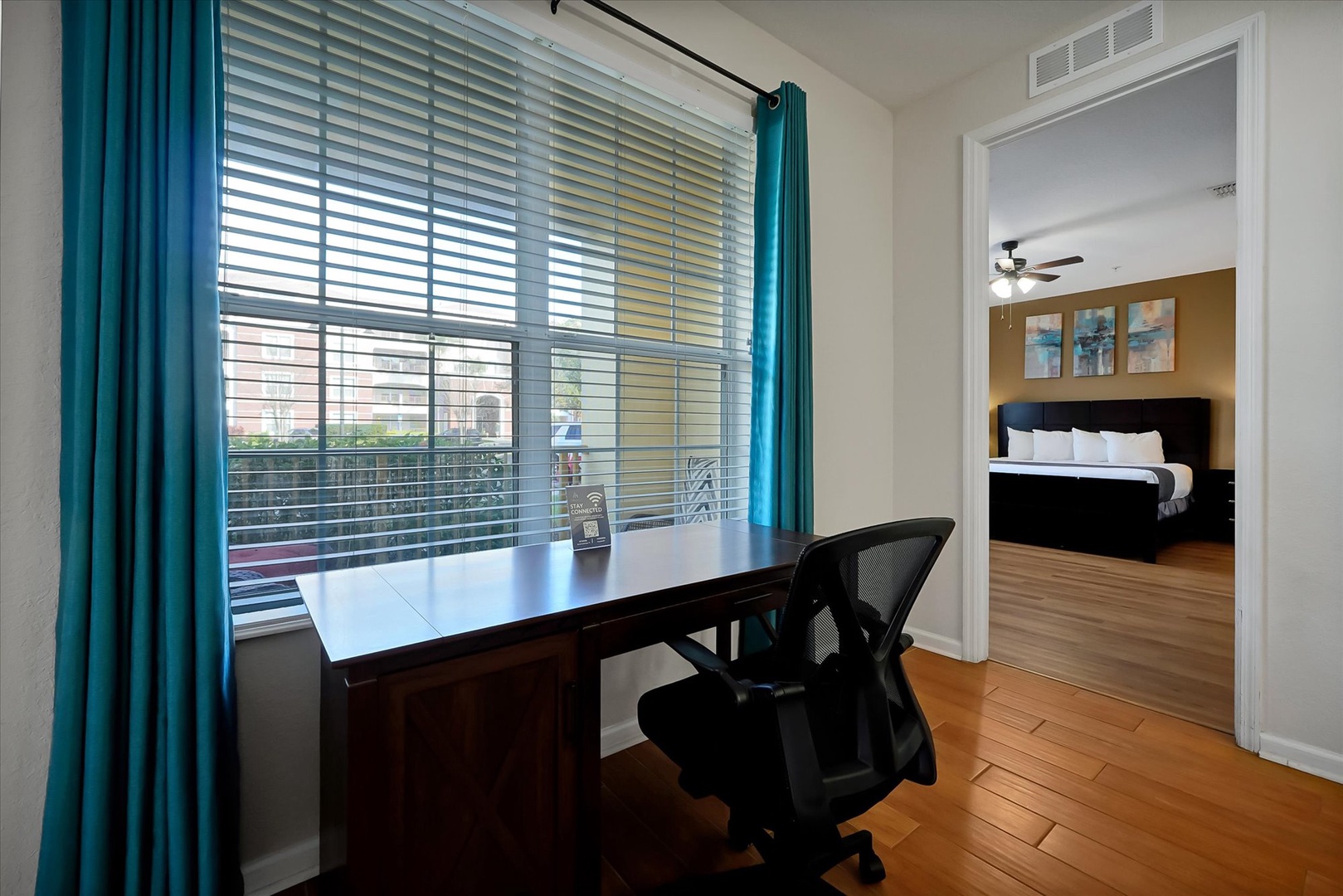 Your dedicated workspace features a sleek desk by the window, where natural light streams through vibrant teal curtains to inspire productivity.