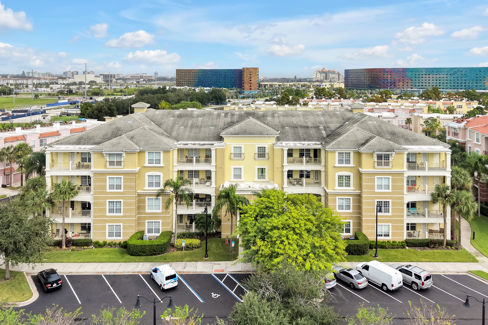 A multi-story yellow residential building with private balconies, surrounded by palm trees and manicured landscaping in a well-established area.