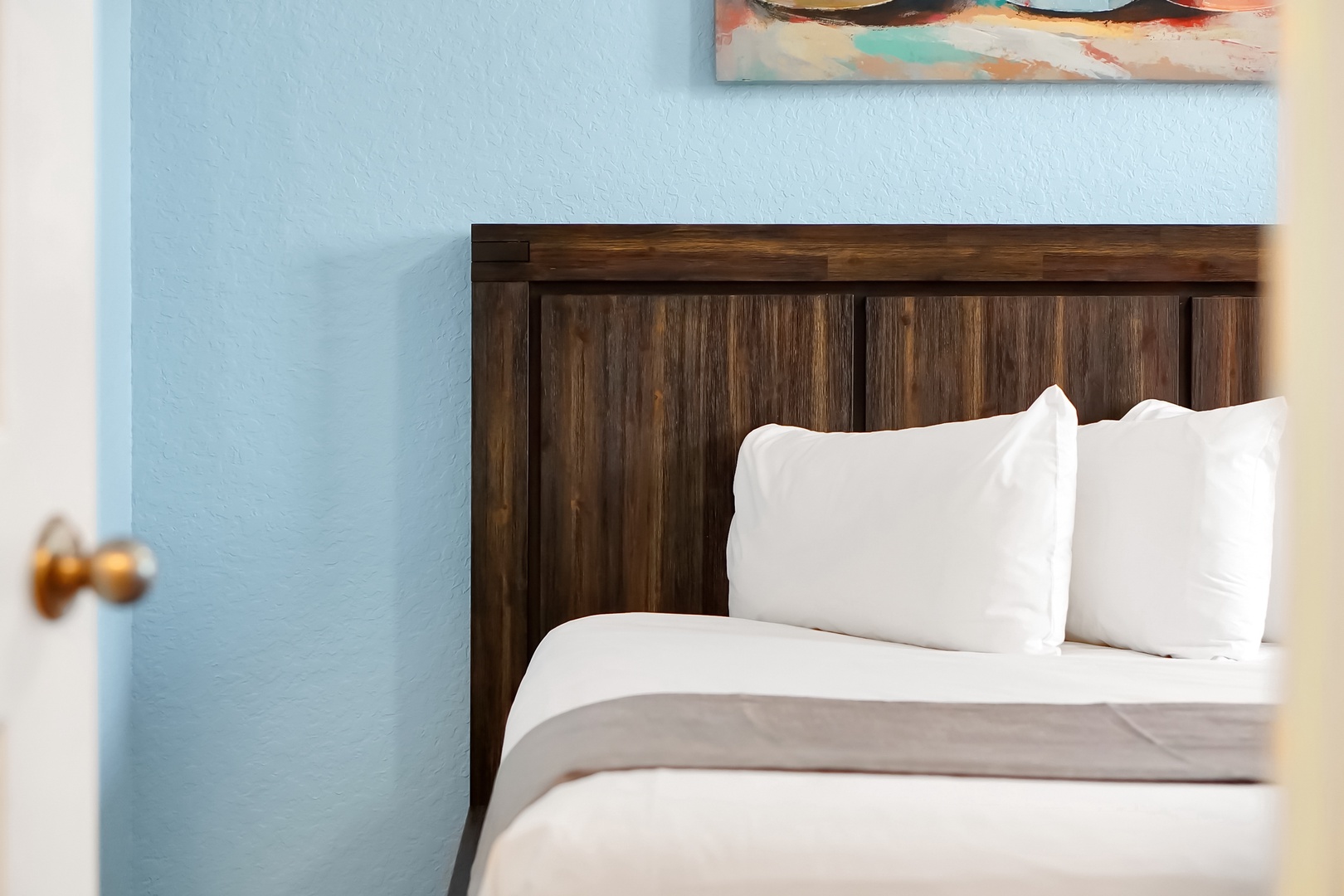 Sink into crisp white linens against this rich wooden headboard, where coastal blue walls create your perfect retreat.