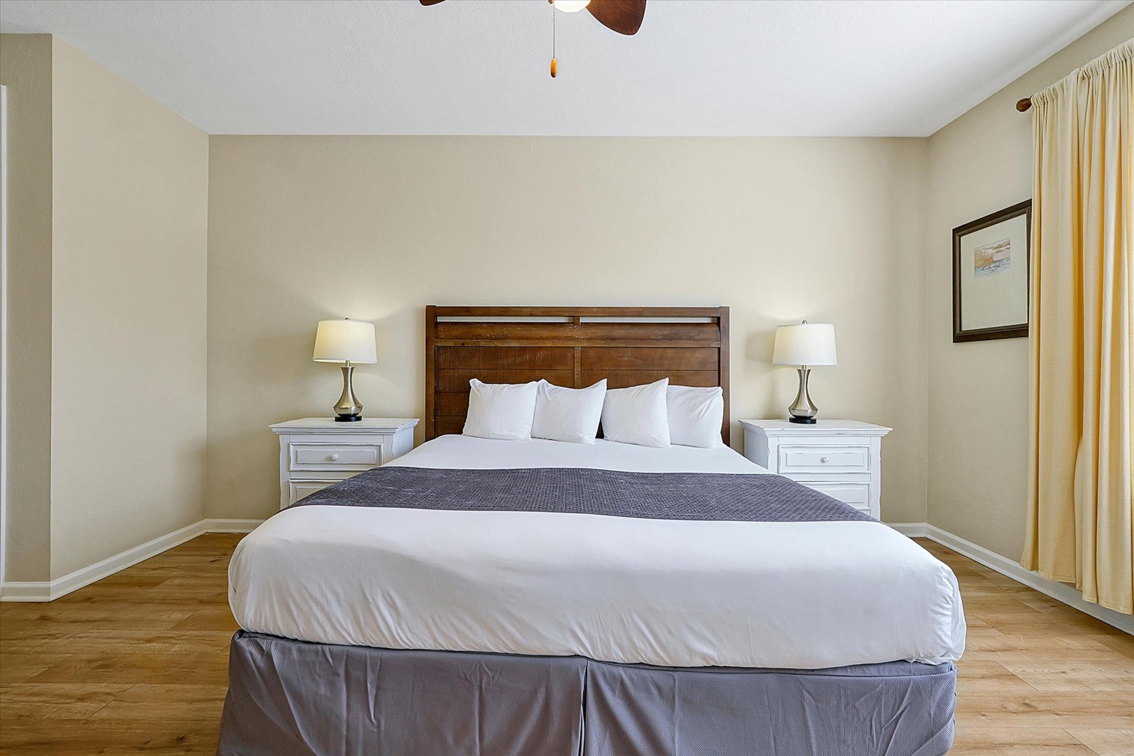 Sink into crisp white linens and fluffy pillows in your serene bedroom retreat, where warm wood floors and soft lighting create the perfect ambiance for rest.