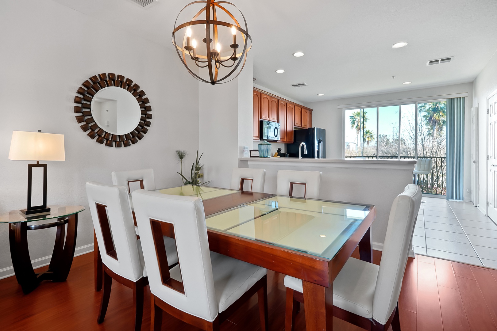 Gather around your elegant dining table with gleaming glass top, surrounded by plush white chairs under stunning chandelier light.