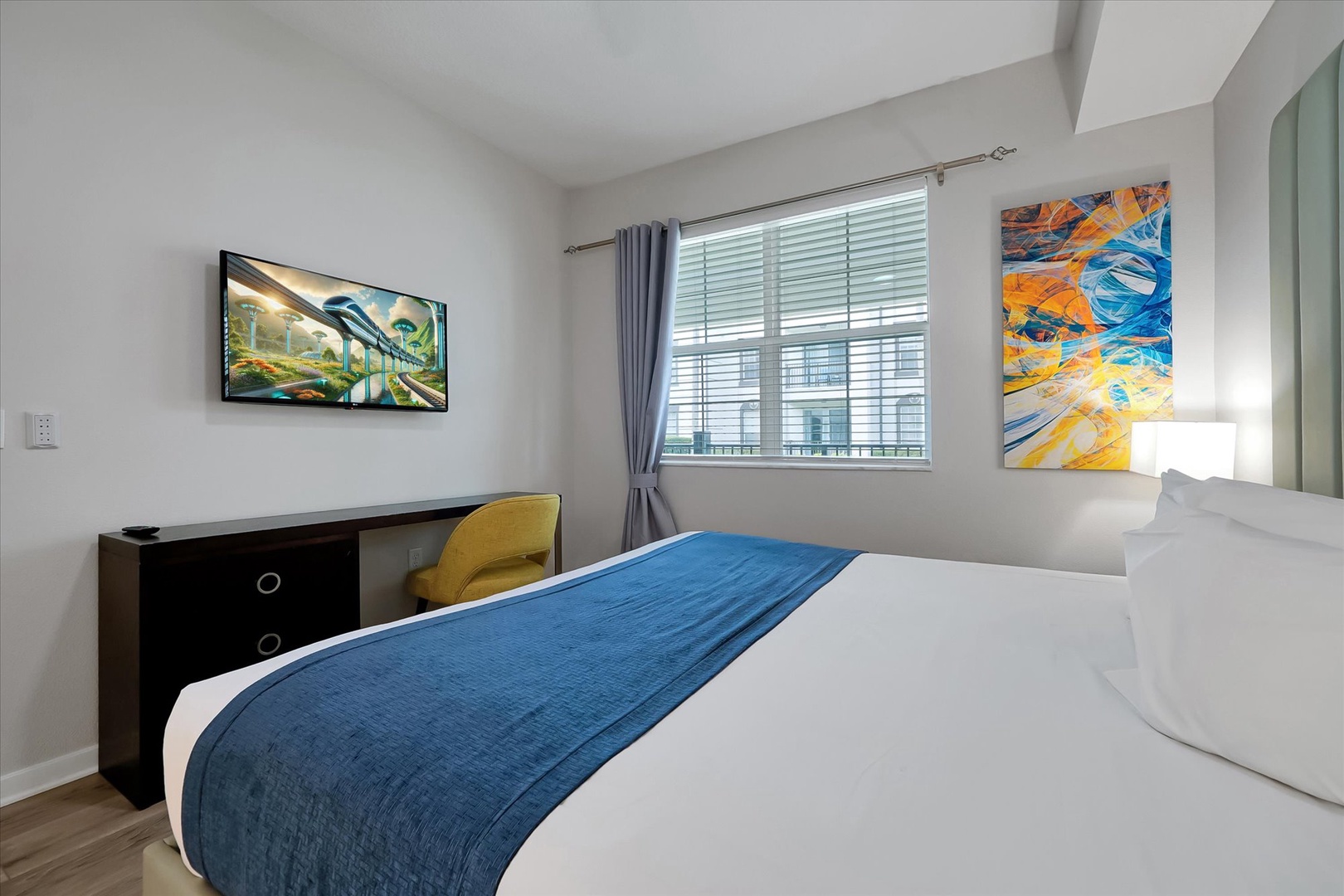 Sink into crisp white linens with a vibrant blue accent throw in your bright, art-filled bedroom featuring modern amenities.