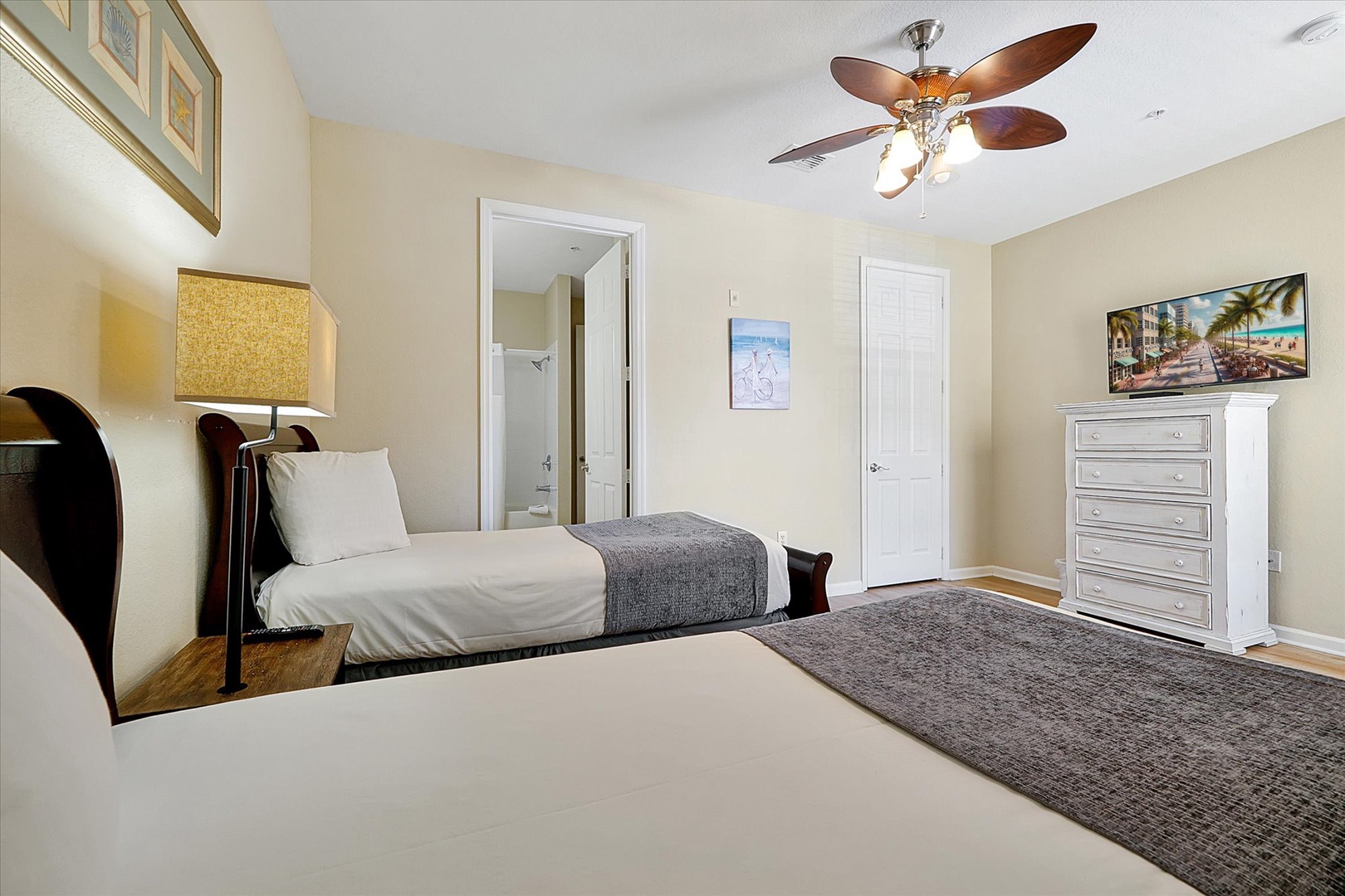 Unwind in your spacious bedroom featuring twin beds with soft linens, tropical artwork, and a gentle ceiling fan for your perfect night's rest.