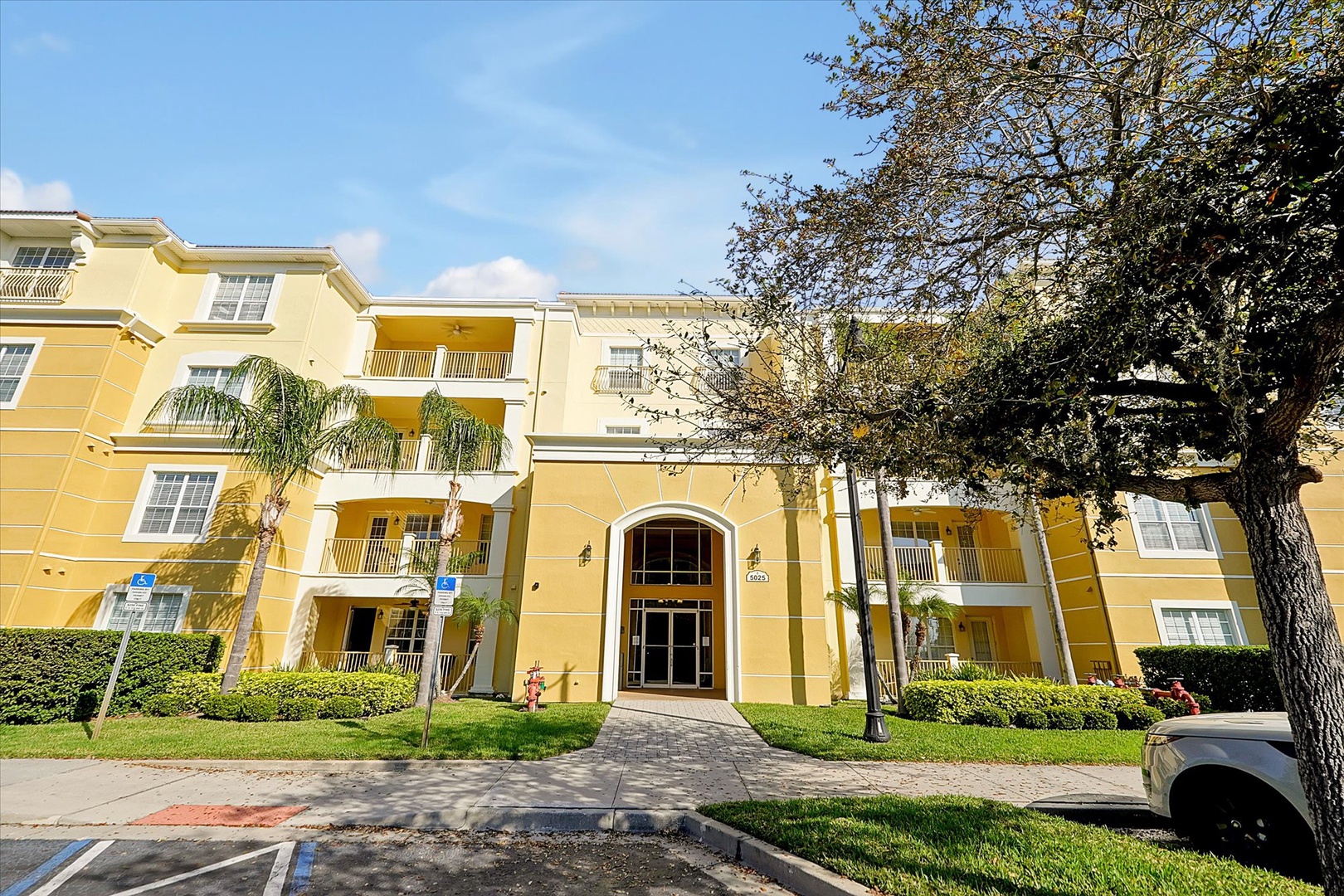 Bright yellow Mediterranean-style building with palm trees and manicured grounds creates a welcoming tropical atmosphere in this peaceful residential setting.