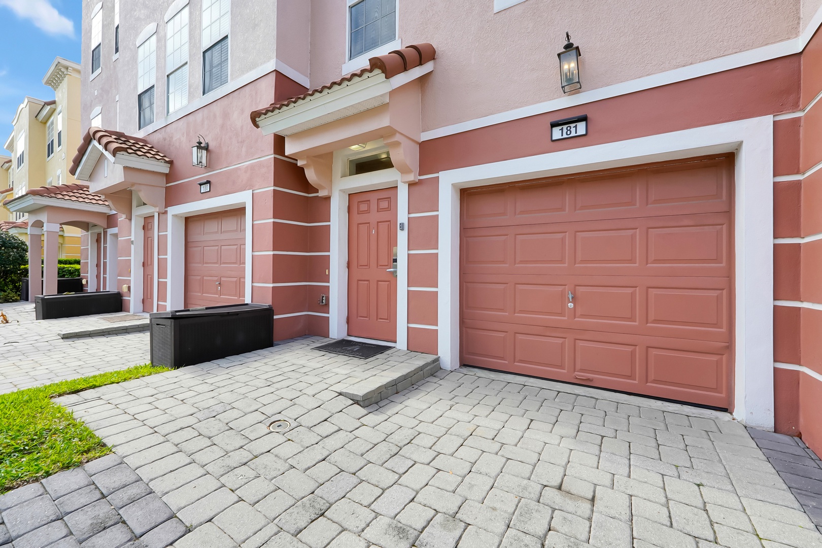 Mediterranean-style townhomes with distinctive coral facades and private two-car garages, featuring elegant architectural details and paved driveways in a modern residential development.