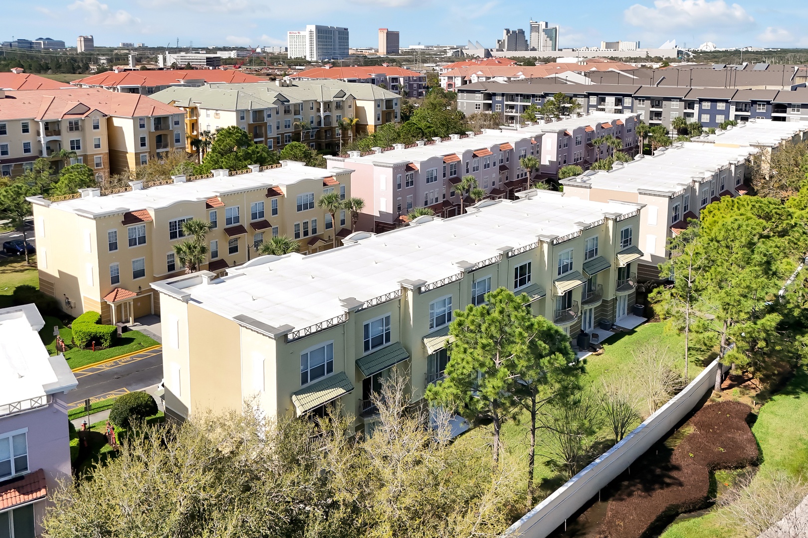 Aerial view of modern townhomes and residential developments in a vibrant community setting with city skyline backdrop.