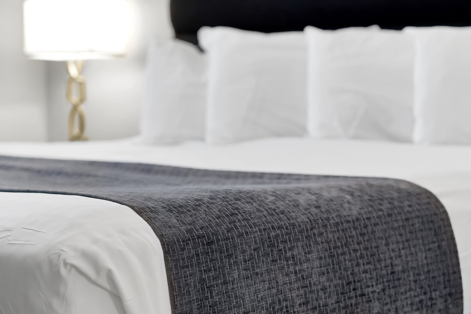 Sink into crisp white linens with a stylish charcoal runner adding a sophisticated touch. Your bedside lamp creates a warm, welcoming glow for peaceful evenings.