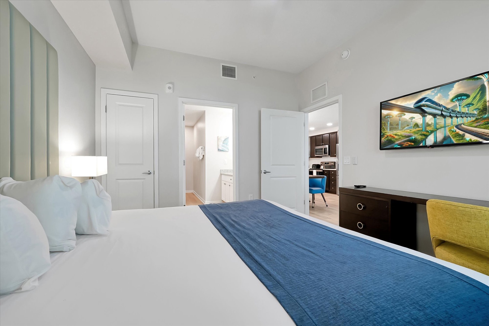 Sink into crisp white linens with pops of ocean blue in your stylish bedroom, featuring modern furnishings and sleek entertainment setup.