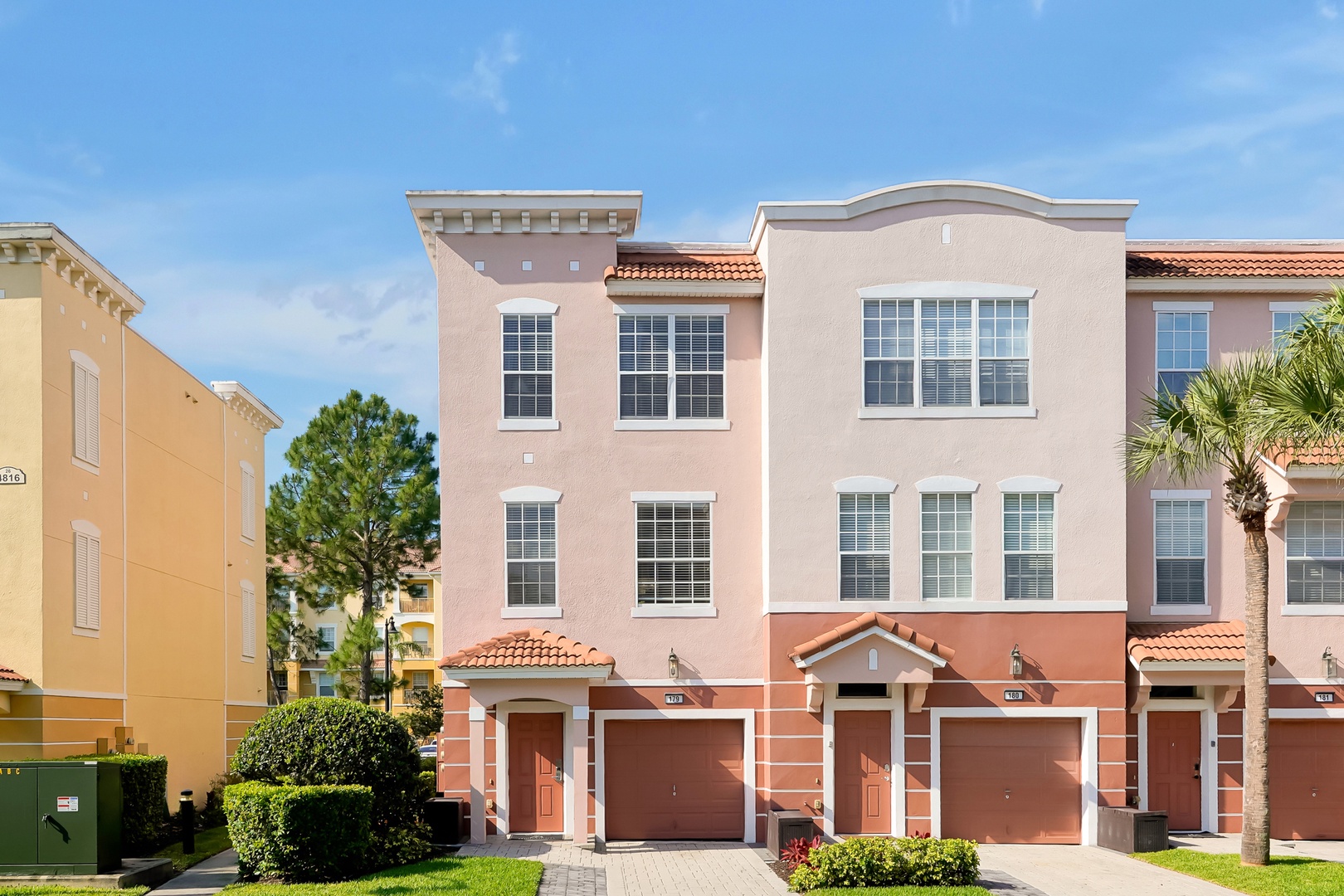 Modern Mediterranean-style townhomes featuring three-story living with attached garages and vibrant coral-pink exteriors in a well-maintained residential community.