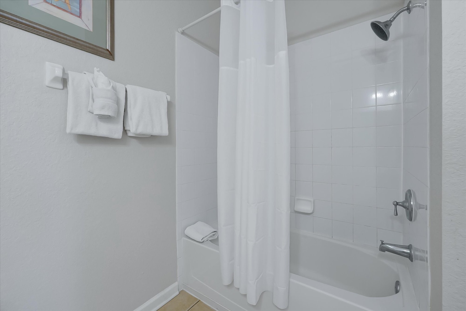 Step into your private bathroom featuring a spacious tub-shower combo with fresh white linens and modern tile work for your comfort.