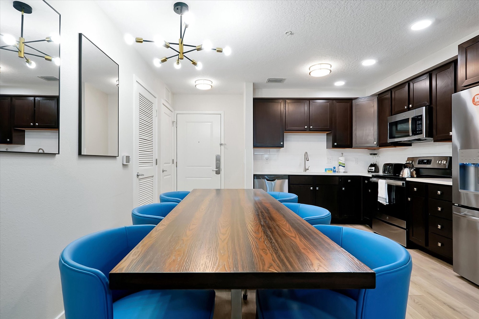 Gather around your sleek dining table where wood grains flow like river currents, surrounded by vibrant blue chairs in your modern kitchen.