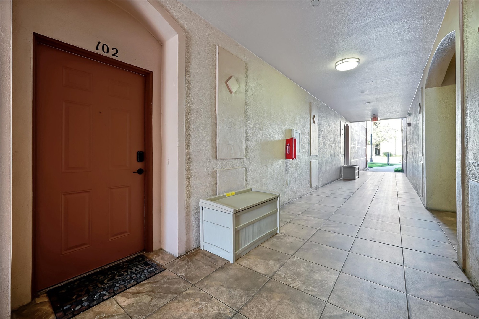 A well-lit hallway leads to your private entrance, marked room 102, with convenient seating and clear directional signage throughout.