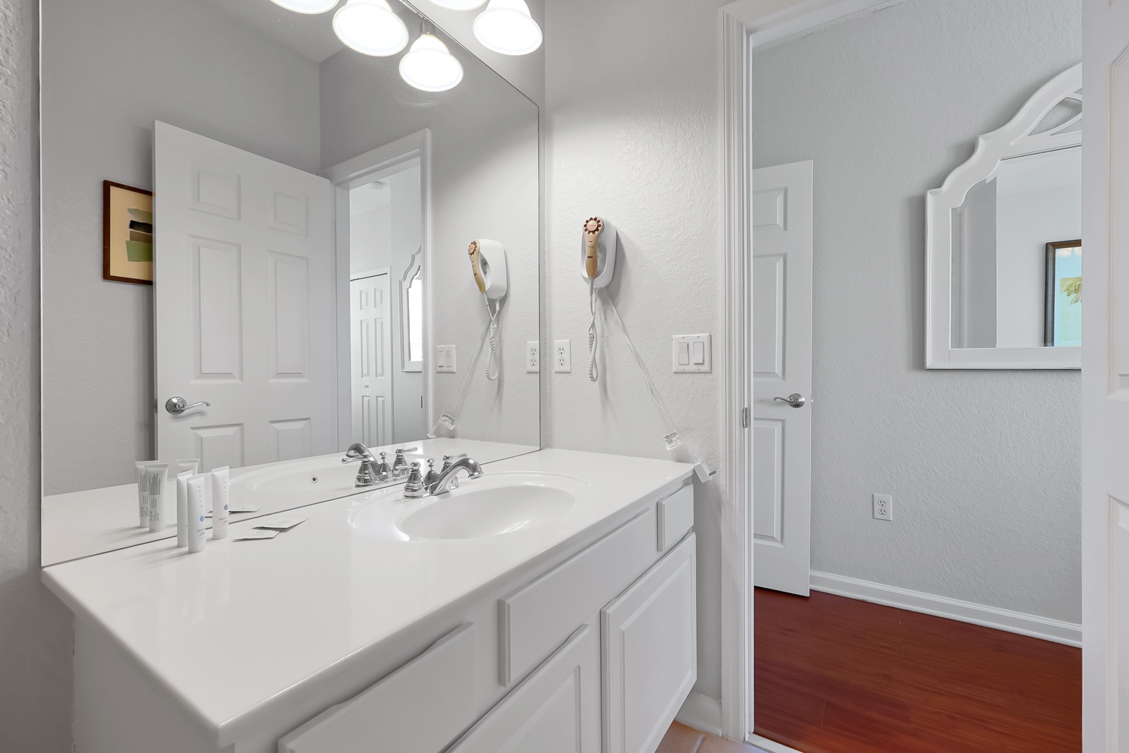 Refresh in your pristine white bathroom with modern vanity, bright lighting, and convenient hair dryer for easy mornings.