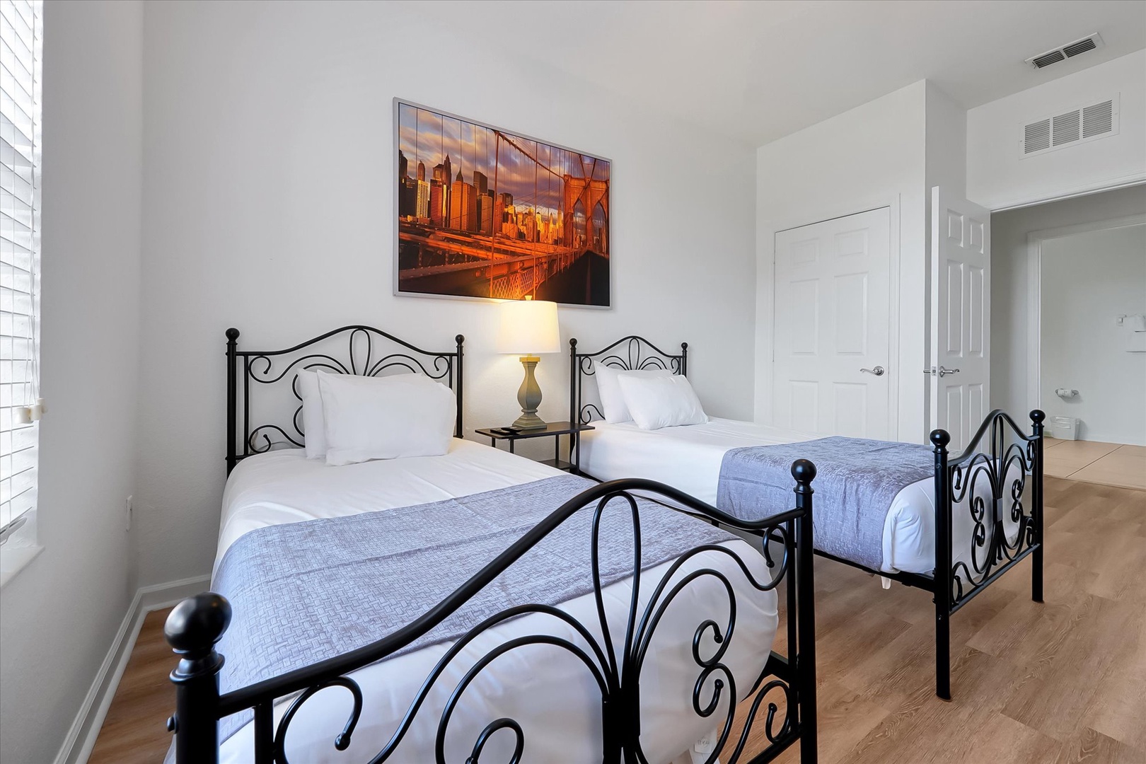 Your peaceful twin bedroom with decorative iron beds and city artwork creates the perfect space for restful nights.