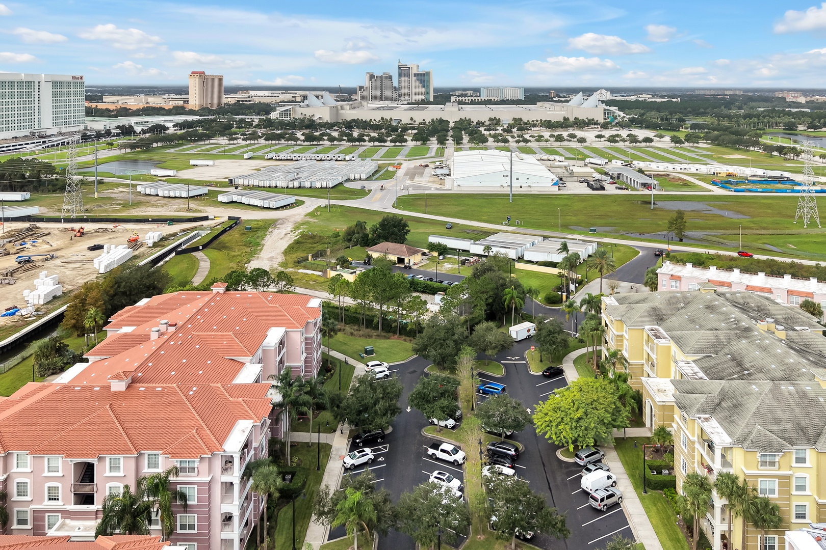 Aerial view of the resort property and surrounding area, showcasing the lush green spaces, parking facilities, and nearby recreational fields with Orlando's skyline in the distance.