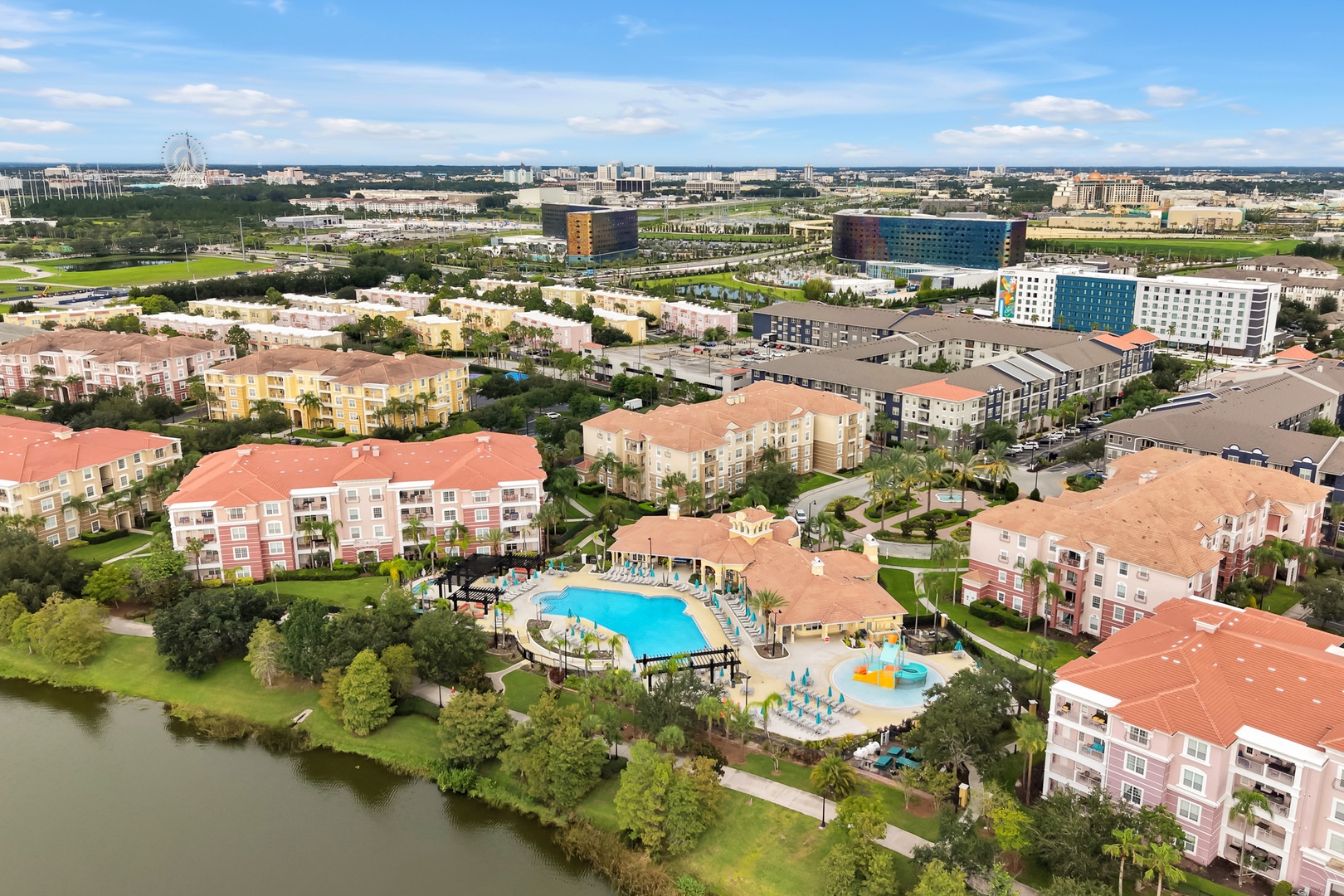 Aerial view of the resort property showcasing Mediterranean-style buildings, a sparkling pool area with waterslides, and convenient proximity to Orlando's attractions including theme parks visible on the horizon.