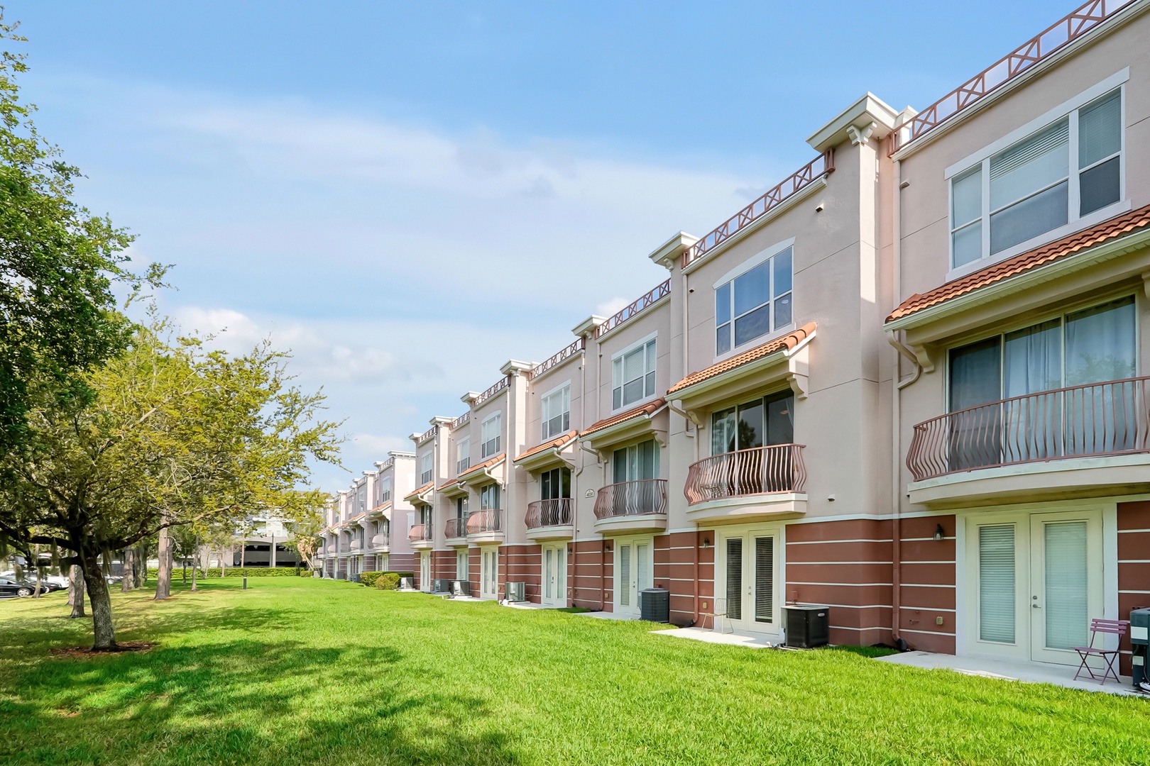 Modern townhome complex with private balconies overlooking manicured green lawns and tree-lined grounds.