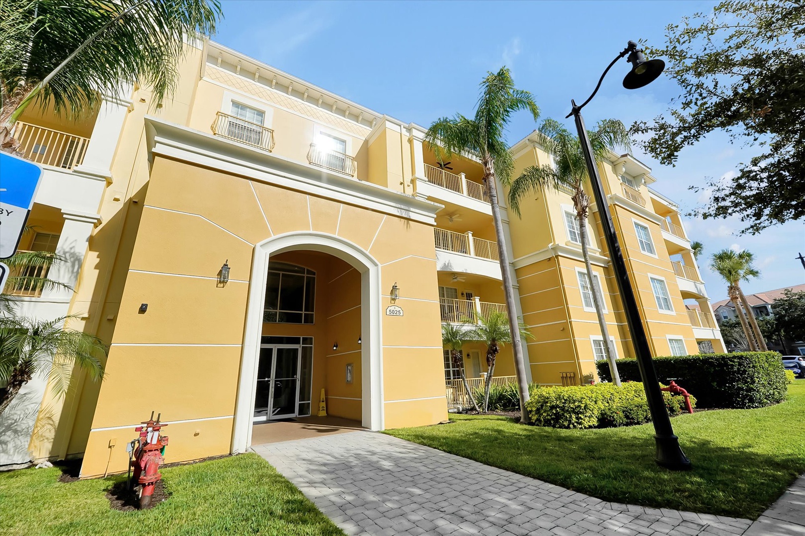 Bright yellow resort building features tropical landscaping and Mediterranean architecture with palm trees and manicured lawns.