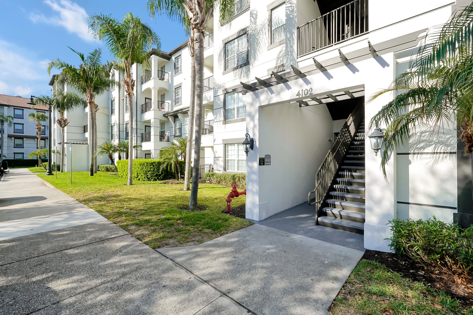 Modern apartment complex entrance with tropical palm trees and manicured landscaping in a peaceful residential setting.