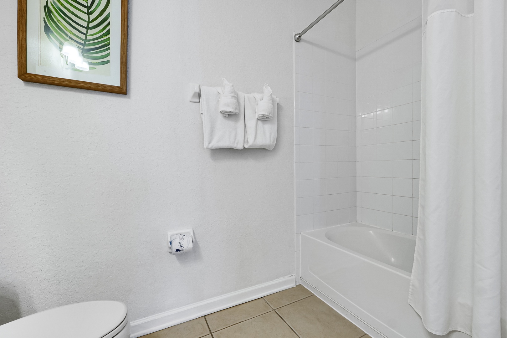Your private bathroom features a tub-shower combo with fresh towels waiting, plus a charming botanical print that adds a natural, calming touch.