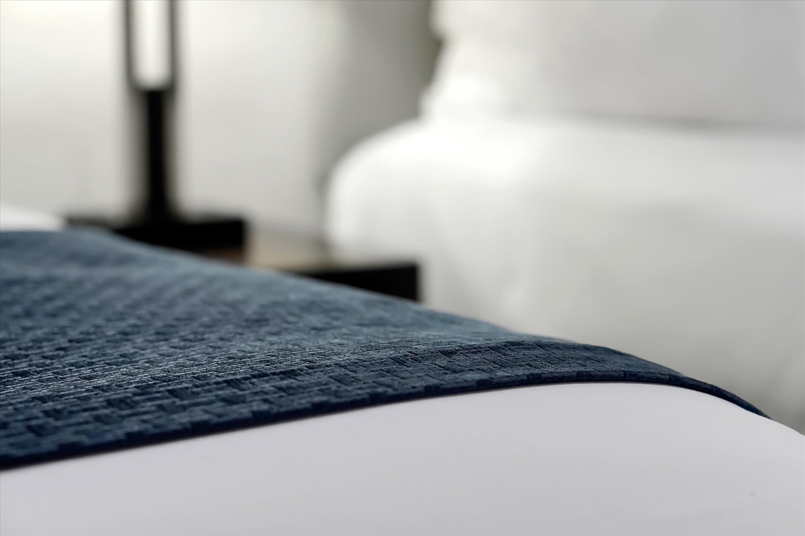 Sink into your cozy bed with crisp white linens and a textured navy throw, perfectly positioned near the bedside lamp for evening reading.